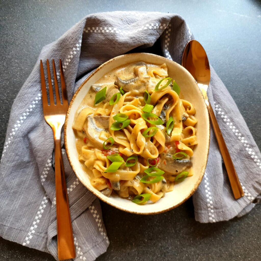 Close-up of a creamy mushroom pasta dish garnished with green onions on a table set for dinner.