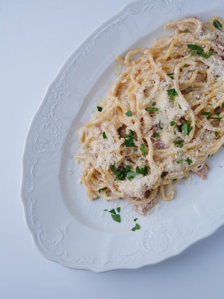 Delicious spaghetti carbonara topped with parmesan cheese and garnished with parsley on a white plate.